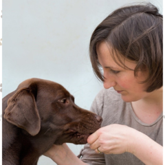 Dr Eleanor Raffan sitting with a chocolate brown labrador dog. One hand is stroking the dog, the other is feeding the dog a treat. 