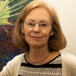 Professor Christine Holt seated next to a microscope, gently smiling at the camera