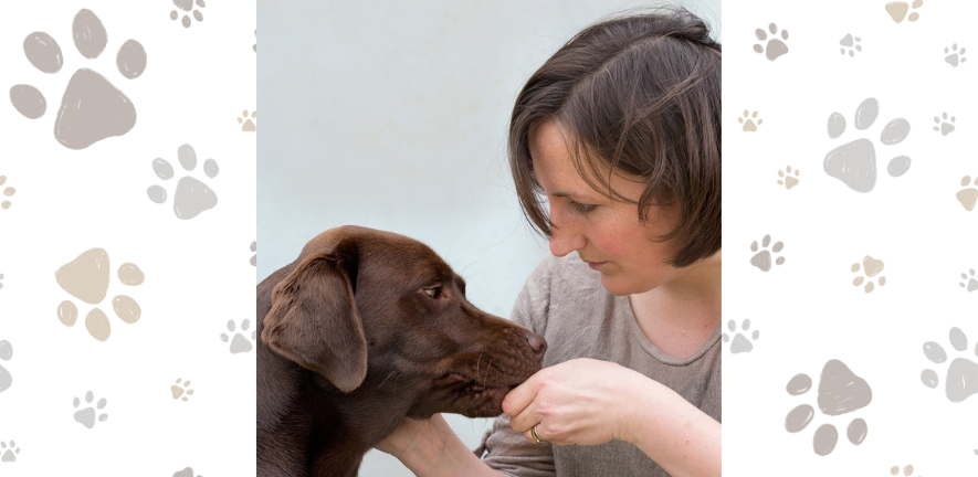 Dr Eleanor Raffan sitting with a chocolate brown labrador dog. One hand is stroking the dog, the other is feeding the dog a treat.