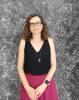 Dr Guela Hanin stands, facing the camera. She is standing in front of a grey background and she is smiling at the camera